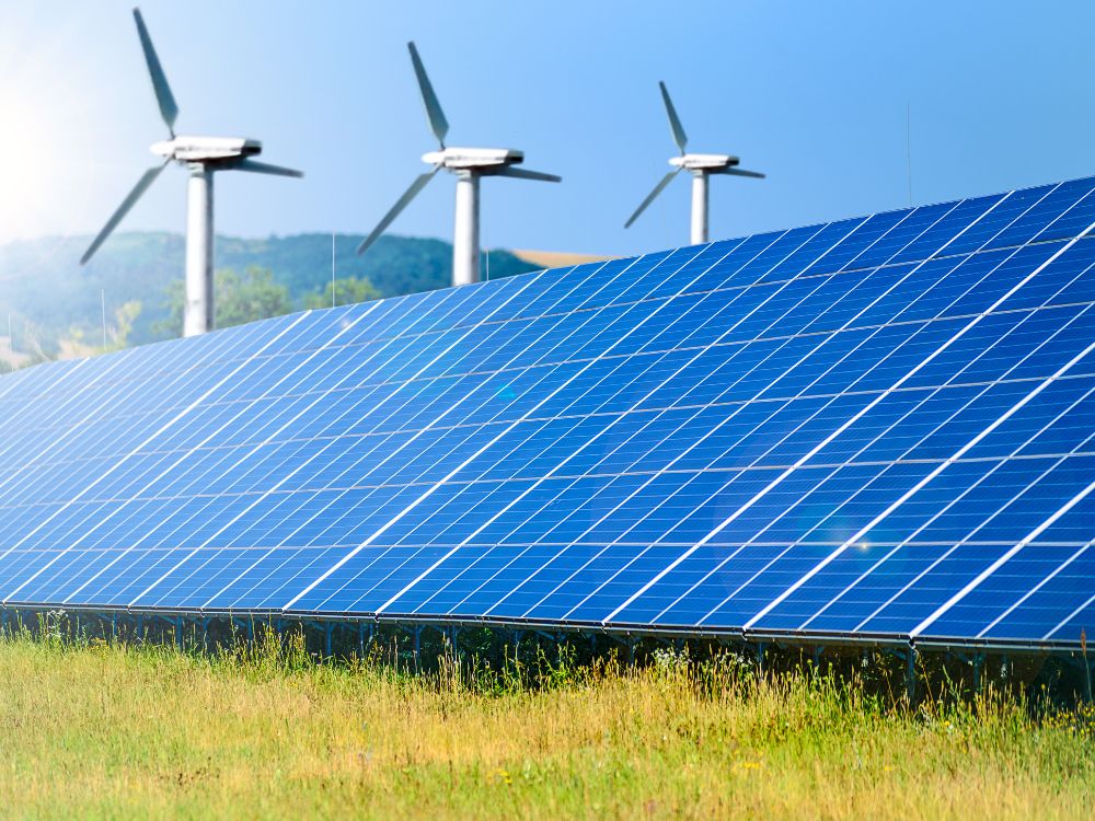Painéis solares em campo com turbinas eólicas ao fundo, representando fontes de energia limpa e renovável como alternativas sustentáveis.