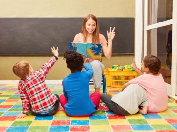Coordenadora pedagógica interage com crianças em sala colorida, promovendo aprendizado lúdico e participação ativa dos alunos.